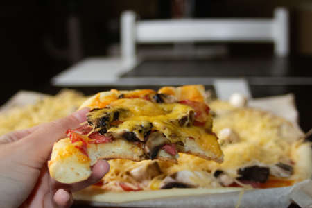 Defocus closeup piece of pizza with freshly grated mozzarella cheese. Woman holding pizza. Copy...