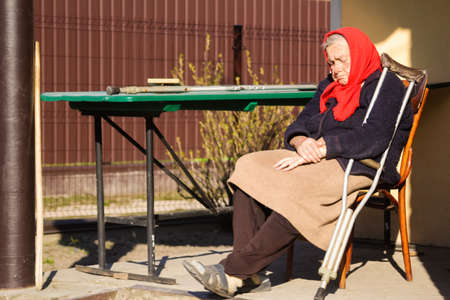 Defocus ukrainian elderly woman in red shawl with crutches sleeping outside. Woman 90 years old. Alone person. Sick and homecare. Out of focus.の写真素材