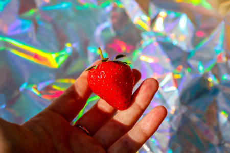Defocus close-up hand holding ripe red strawberry on modern hologram background. Fruits and berries. Harvest and crop concept. Organic. Trendy gradient. Out of focus.の写真素材