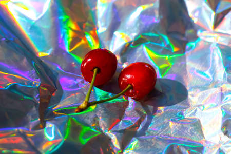 Defocus close-up two red wet sweet cherries with tail and leaves on modern hologram background. Fruits and berries. Harvest and crop concept. Organic, eco. Out of focus.の写真素材