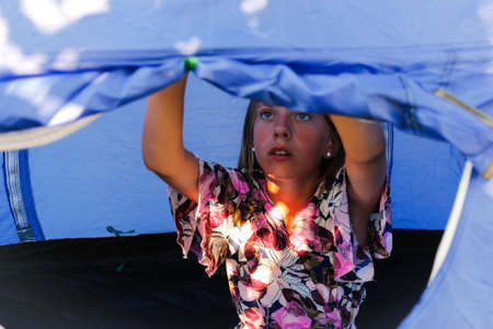 The girl sitting comfortably inside a camping blue tent behind a mesh anti-mosquito window, she...
