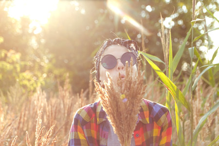 Defocus teen or preteen girl walking on nature background. Little kid girl holding bunch of pampas grass and blowing. Blurred reed on foreground. Hipster, generation z. Sunny, sunset. Out of focus.の写真素材