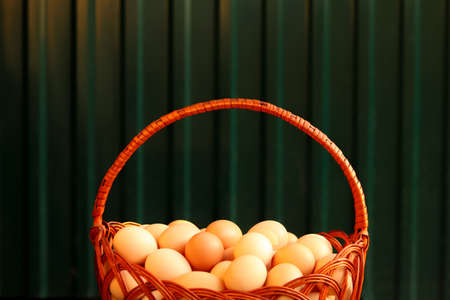 Many eggs in basket. Closeup whole basket of brown organic eggs on green modern background. Poultry farm. Eco agriculture, fresh group egg, import, export. Closeup. Sunny. Nobody. Wooden detail.の写真素材