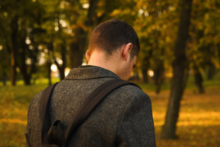 Defocus young man holding phone. Man using smart phone in autumn park. Typing text message or...