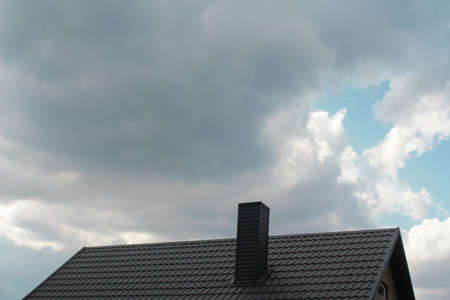 Defocus steel roof on dark sky background. Dark rain clouds above the modern roof. Roof with new black roofing tiles double flap on residential property. Out of focus.の写真素材