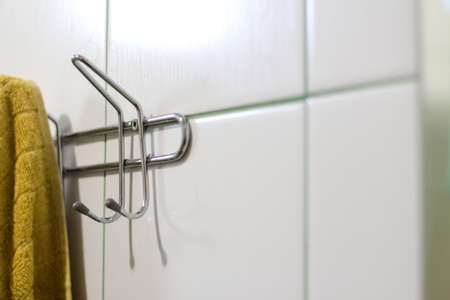 Defocus mustard towel hanging on hook. Metal sticky towels hanger for bathroom tiled wall. Closeup...