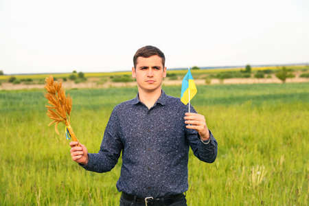Defocus young ukrainian man portrait. Bouquet of ripe golden spikelets of wheat tied on the meadow...