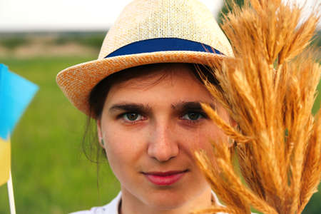 Defocus female hand holding and showing ukrainian passport, flag and wheat spikes of wheat tied and flag on the green nature background. Ukrainian women. Vyshyvanka. Freedom. Closeup. Out of focus.の写真素材