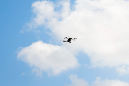 Defocus war drone. Drone flying in a blue sky. The black army unmanned aerial vehicle with four propellers and blades is on the blue sky background. White clouds. Out of focusの写真素材