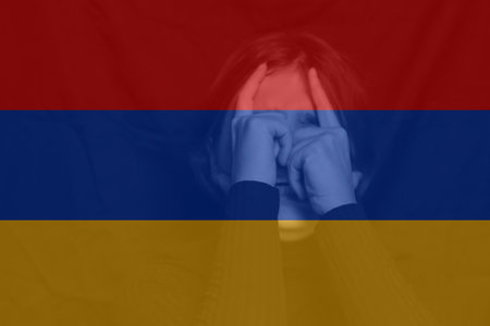 War between Armenia and Azerbaijan. Young woman with sad sight looking at camera. Woman screaming. Armenia flag. Face of depression. Caucasian woman. Crisis. Out of focus.の写真素材