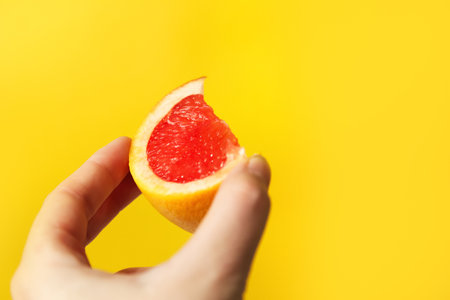Defocus female hand holding piece of a red grapefruit. Healthy food concept. Fresh orange juice. Vegan, vegetarian concept. Banner with copy space. Out of focus.の写真素材