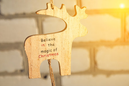 Christmas reindeer toy on brick background, sunny. Wooden small model winter deer toy on white background. Christmas deer hanging. Copy space. Winter holiday concept. Mock-up for design.の写真素材