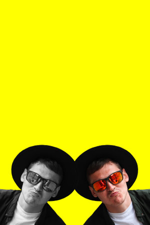 Two funny man. Smiling fashion man. Portrait of handsome smiling stylish hipster model. Man dressed in red polarization sunglasses and hat. Fashion male on yellow background. Copy space.の写真素材