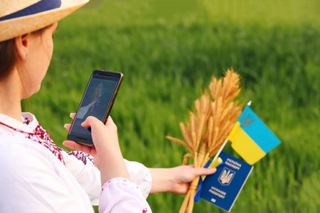 Defocus female hand holding ukrainian passport, flag and wheat spikes of wheat tied and flag on the...