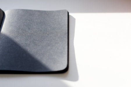 Defocus blank black notebook on a white table, mockup photo. Blank black cover template with copy space for design. Black minimal design concept. Shadow. Out of focus.の写真素材