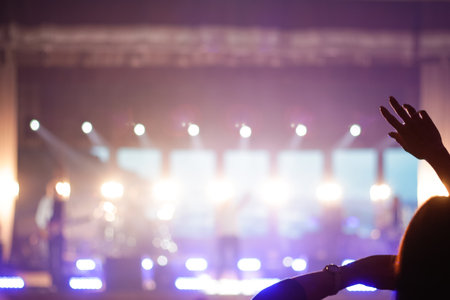 Defocus silhouette of one woman raise hand up in music concert with purple and white color spotlight on stage background. Out of focus.の写真素材