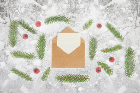 Defocus eco craft envelope, letter to Santa. Frame of fir branch or spruce branch and red berries on snowy background. Fir tree branches. Christmas greeting card. Top view. Out of focus.の写真素材