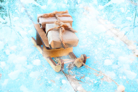 Defocus Xmas gift composition. Wrapped craft vintage gift boxes lying wooden toy sled on blue snowy...