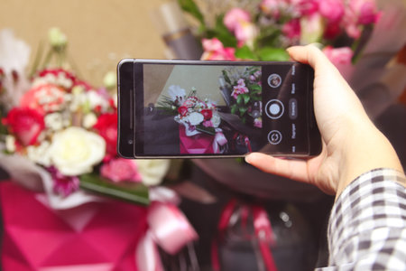 Defocus male hand taking photo of colorful roses with cell, mobile phone. Woman with a gift of flowers. Female florist with many roses bunches and bouquets. Florist. Out of focus.の写真素材