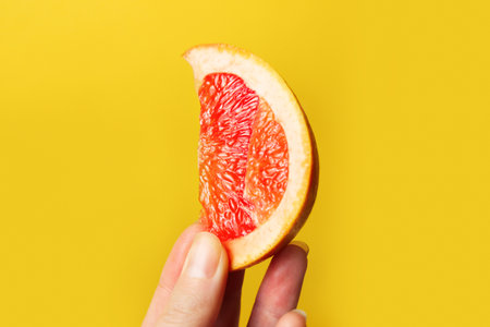 Defocus female hand holding piece of a red grapefruit. Healthy food concept. Fresh orange juice. Vegan, vegetarian concept. Banner with copy space. Citrus fruit. Slice. Out of focus.の写真素材