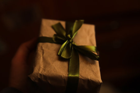 Defocus craft eco gift box with magical light against dark light background. Dark night. Hand holding present. Out of focusの写真素材
