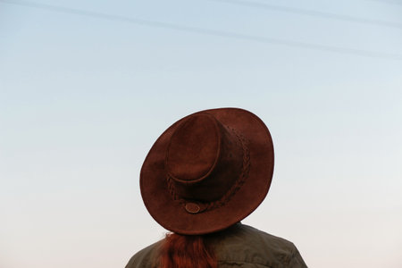 Back view of a young shirtless woman wearing a cowboy hat. Young cowboy looking on blue sky away. Adventure western concept. Out of focusの写真素材