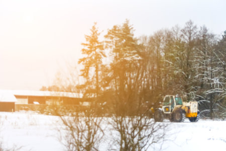 Defocus tractor clean snow sunny flare. Tractor cleaning snow in field. Big yellow tractor cleans up snow from the road and loads it into the truck. Out of focus.の写真素材
