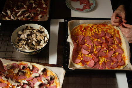Defocus ingredients for pizza on dough. Female and male hand cooking. Red tomato sauce, sausages, sweet corn, mushrooms. Homemade pizza. Base of Margarita. Home culinary. Top view. Out of focusの写真素材