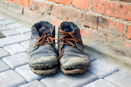 Dirty old shoes on paveng floor. A pair of dirty boots. Old worn leather shoes with variegated brown laces. The concept of poverty, homelessness, lack of money. Selective focus.の写真素材