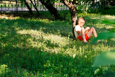 Happy child teen boy sitting on green grass outdoors in spring park or garden. Happy child boy on meadow in summer in nature. Dreaming concept. Copy spaceの写真素材