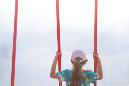 little girl swinging on swing on playground. Gray sky. Kids summer game. Girl have fun on summer holiday. Out of focus.の写真素材