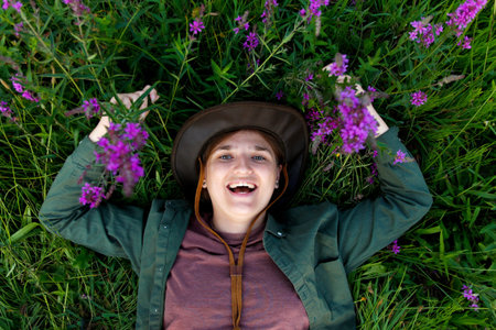 Funny woman lying in summer grass and purple flowers. Wellness. Hello summer. Top view. Summertime. Young woman 20s years smiling. Happy youth. Out of focus.の写真素材