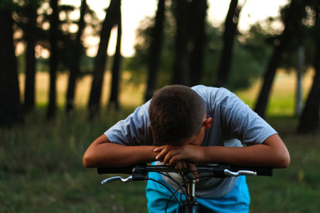 Sad little boy sitting on bicycle near forest. Child cry and hidの写真素材