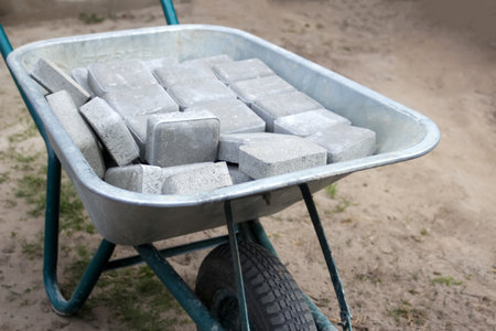 Defocus brick tiles stacked on a wheelbarrow. Gray pavement bricks for pavement road. Stack paving...