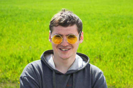Portrait of handsome man wearing yellow sunglasses on a green grass background. Funny man outside....