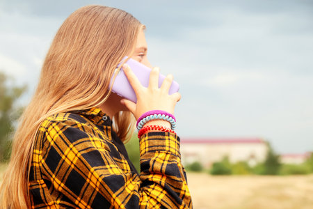 Woman speaking and talking mobile phone on yellow nature background. Blue Smart phone in the purple case. Mobile call. Out of focusの写真素材
