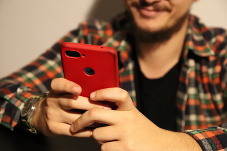 Man holding red smartphone, smiling with phone and using social media. Emphasizing the joy and ease of using modern technology for social interactionsの写真素材
