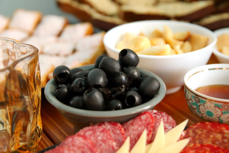 Olives, sausage, and cheese arranged on a serving dish with honey on a rustic table. Mediterranean appetizer spread featuring olives on a serving dish.の写真素材