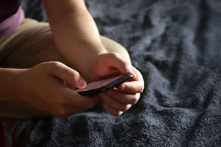 Man typing on phone with hand in dark indoor setting. Mobile device in hand with dark background....
