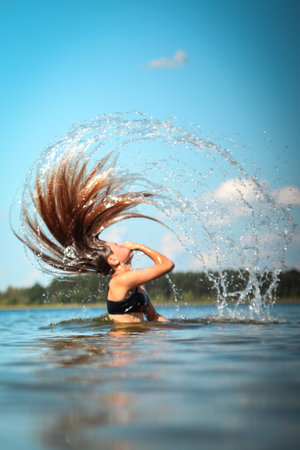 A young woman swimming in the clear blue ocean, her hair flowing in the water as she splashes around. She appears to be enjoying a refreshing summer day, with waves gently splashing around her.の写真素材