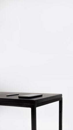 Minimal business background with a white table, vertical orientation. Features a smartphone, pen, and open space, creating a clean and modern look.の写真素材