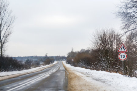 Slippery road warning sign, standing against a cold winter backdrop. Blurred, out of focus background.の写真素材