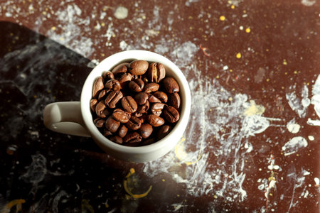 A coffee scene with a white cup filled with coffee beans on a brown and black background.の写真素材