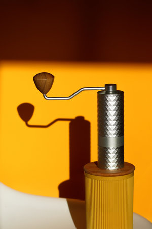 A sleek, modern manual metal coffee grinder with a wooden handle, set against a minimalistic yellow background. Perfect for coffee-related content, minimalist designs.の写真素材