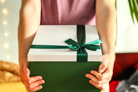 A man hand holding a green gift box with a ribbon, isolated on a neutral background. The composition...