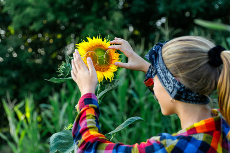 A happy teen girl wearing funny sunglasses in a vibrant yellow sunflower field, enjoying the sun.の写真素材