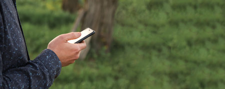 A male hand holding a smartphone with a green background, gently touching the device outside in...