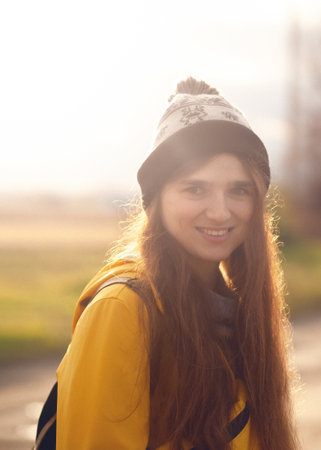 a happy, young woman in her 20s, wearing a yellow raincoat and a hat, with a gentle smile. The...
