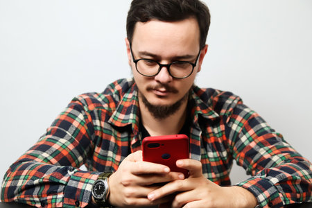 A serious, young man with eyeglasses is on his phone, looking angry. The image, taken indoor, captures a moment of intense business work or a stressful call.の写真素材