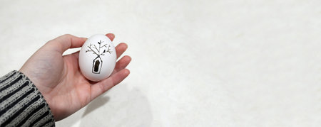 banner with a hand holding a beautiful pysanka Easter egg. The egg, with its intricate black and white pattern and a touch of drawing, represents a timeless tradition from Ukraine.の写真素材